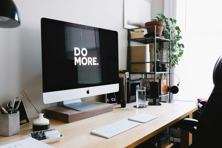 iMac displaying 'DO MORE' on a minimalist wooden desk.