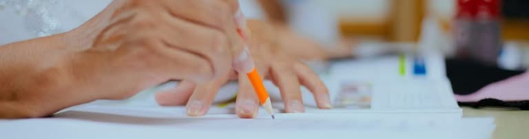 Close-up of hands writing on paper with an orange pencil.