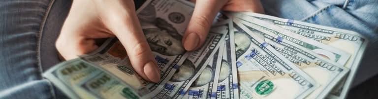 Hands holding and counting a fan of hundred-dollar bills.