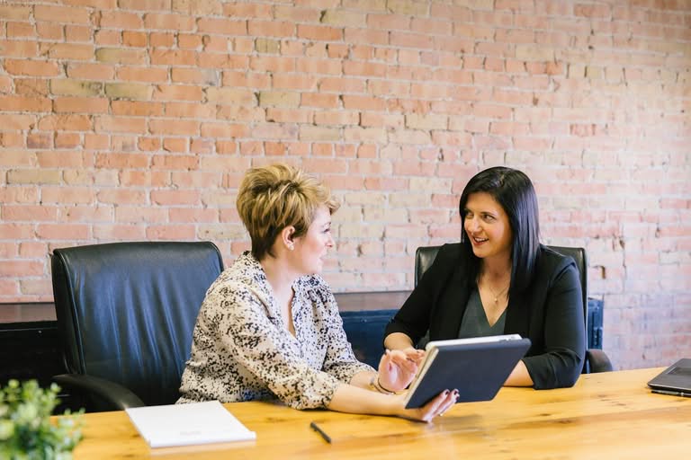 Two professional women collaborating on a tablet in an office.